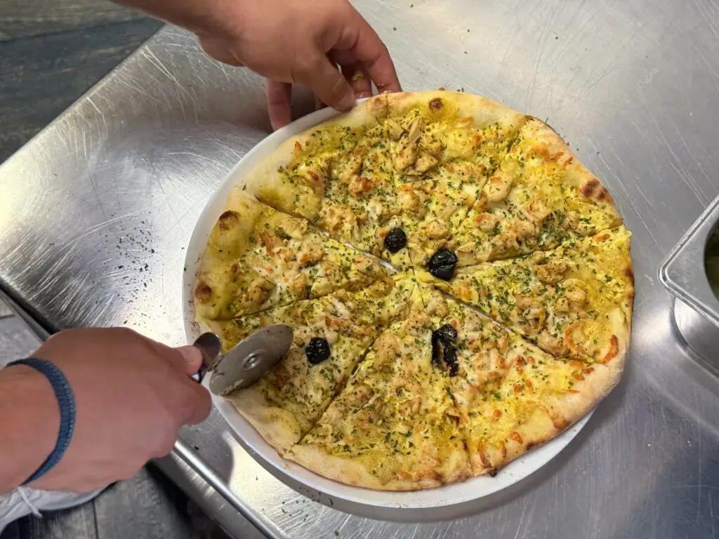 Pizza fraîchement sortie du four en train d’être découpée chez Pizzeria Crest – Pizza Du Coin